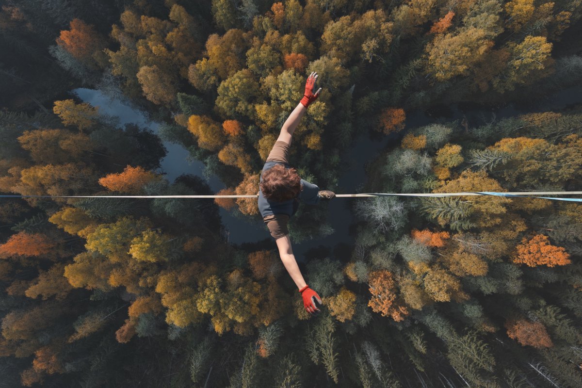 Ein Mensch balanciert auf einer Slackline hoch über einem herbstlichen Wald – Sinnbild für den schmalen Grat zwischen Missverständnis und Konflikt